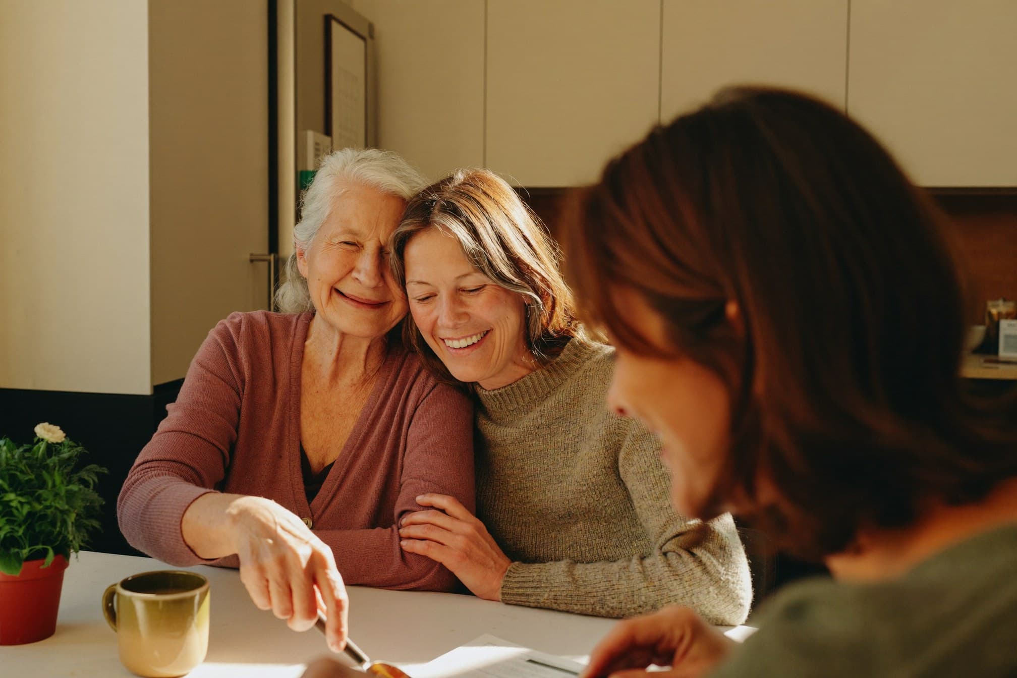 A daughter and her mother laughing together at a kitchen table